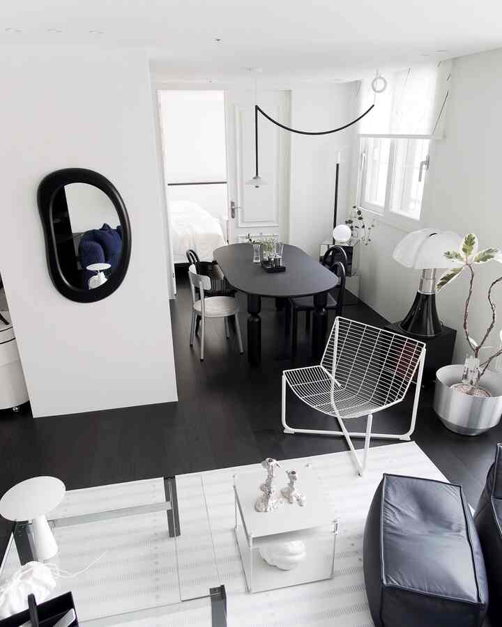 A modern living and dining room in white and black tones, featuring minimalist furniture and plants in a clean space