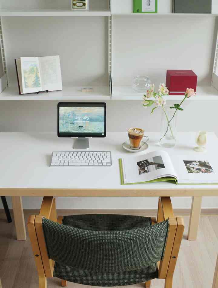 白と木目調が調和した清潔感のあるホームオフィス空間、デスクにはタブレットとコーヒー、花瓶が配置されている