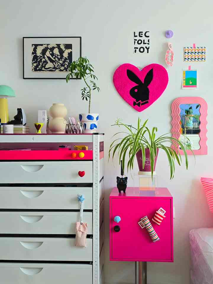 白とピンクのトーンの狭い部屋、ドレッサーと花瓶、多様なウォールデコがある印象的なインテリア