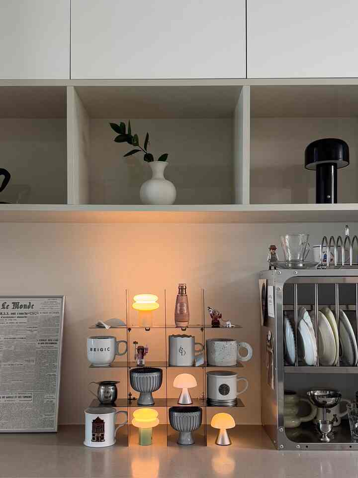 白を基調としたキッチンの棚にテーブルランプやカップ、食器が整然と配置されたミニマルモダンな空間