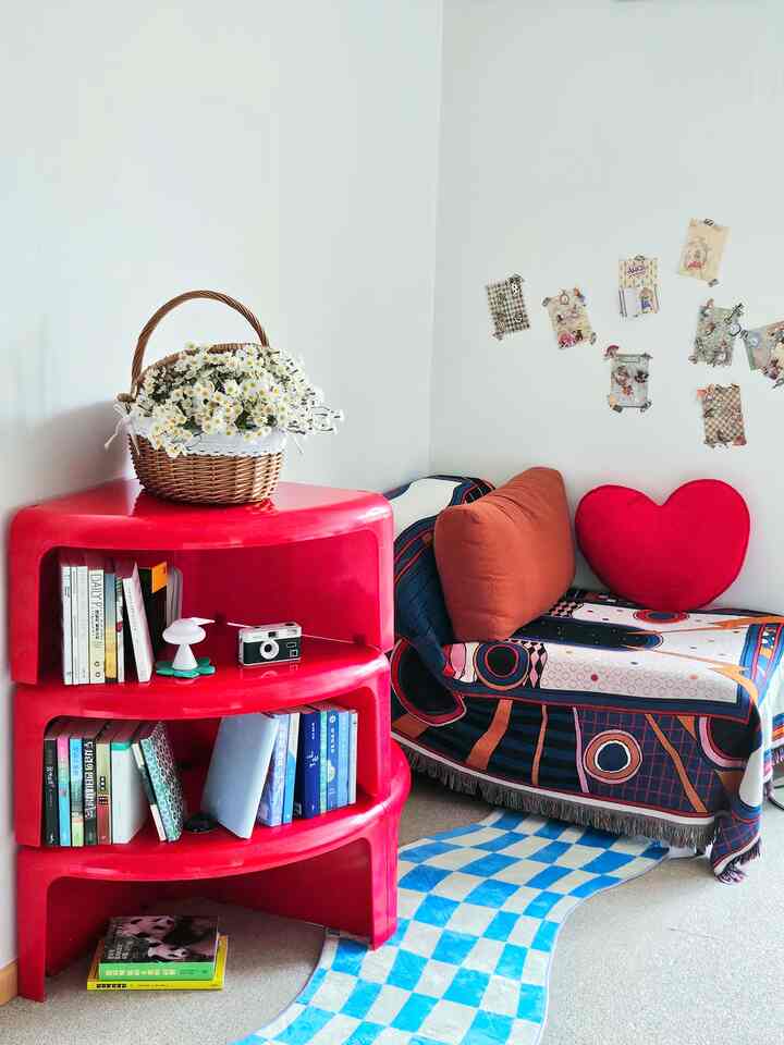 白い壁と鮮やかな赤い本棚がある居心地の良い読書スペース、柄付きのソファと快適なクッションが配置された雰囲気のあるインテリア