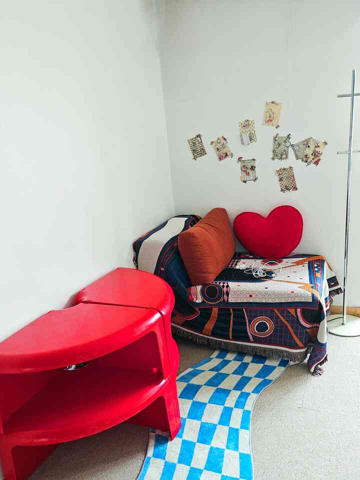 White-walled living room featuring a red corner storage unit, cozy sofa with cushions, and checkered rug offering warm ambiance