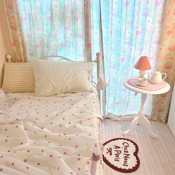 柔らかなホワイトとピンクのトーンの寝室、ハート形のラグと小さな円形テーブルが配置された温かみのある空間