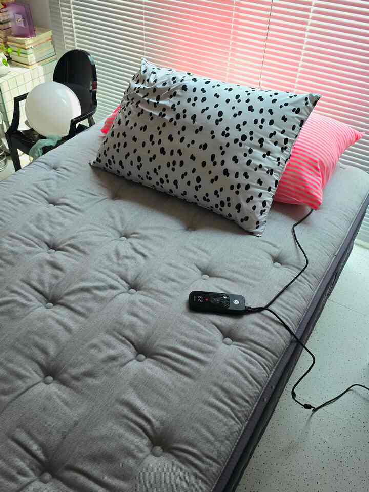 グレーのマットレスと白地に黒のドット柄の枕、ピンクの枕が置かれたモダンな6畳の寝室、背景にピンクのブラインドが配置された印象的な空間