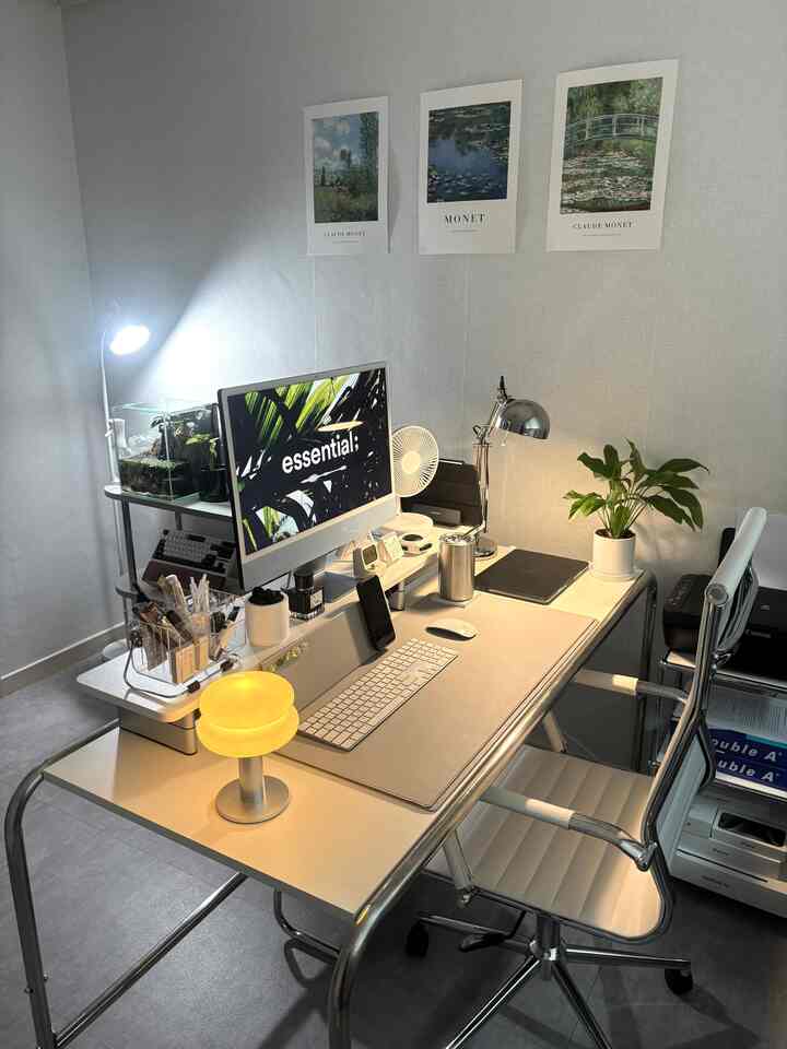 ホワイトとグレーの色調の小さなホームオフィス、ミッドセンチュリーモダンのスチールデスクとオフィスチェア、iMacと照明が配置された印象的な空間