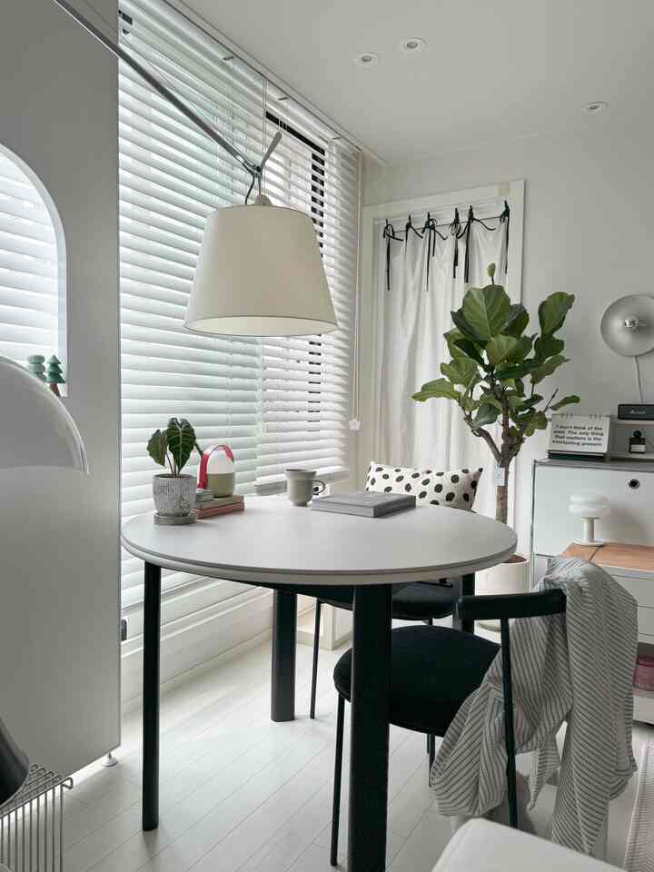 Bright white and black round dining table in a living room space, natural lighting and greenery create a natural atmosphere