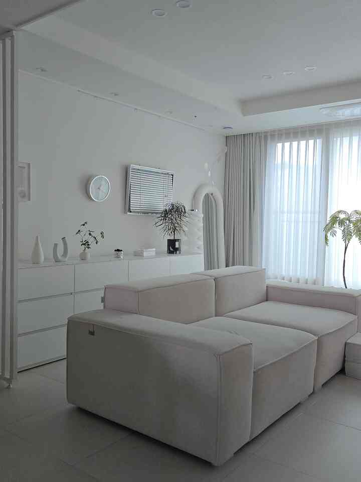 White and natural toned living room featuring a large sofa and storage cabinet, creating a minimal and spacious atmosphere