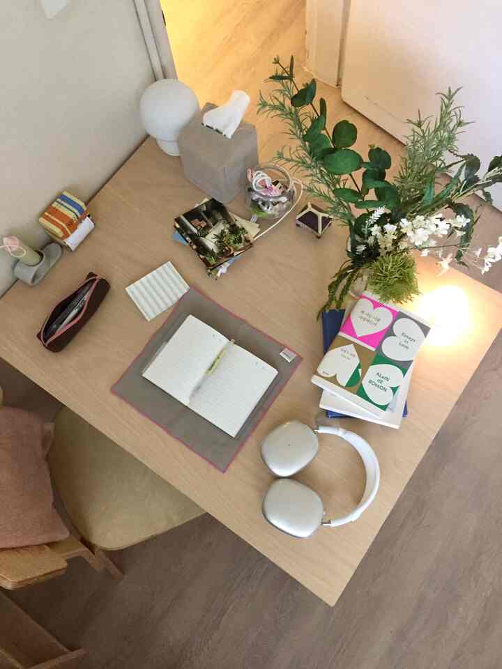 明るい木目調のデスクと椅子が配置されたコンパクトなワンルーム、植物と花瓶が置かれた自然な雰囲気のデスクインテリア