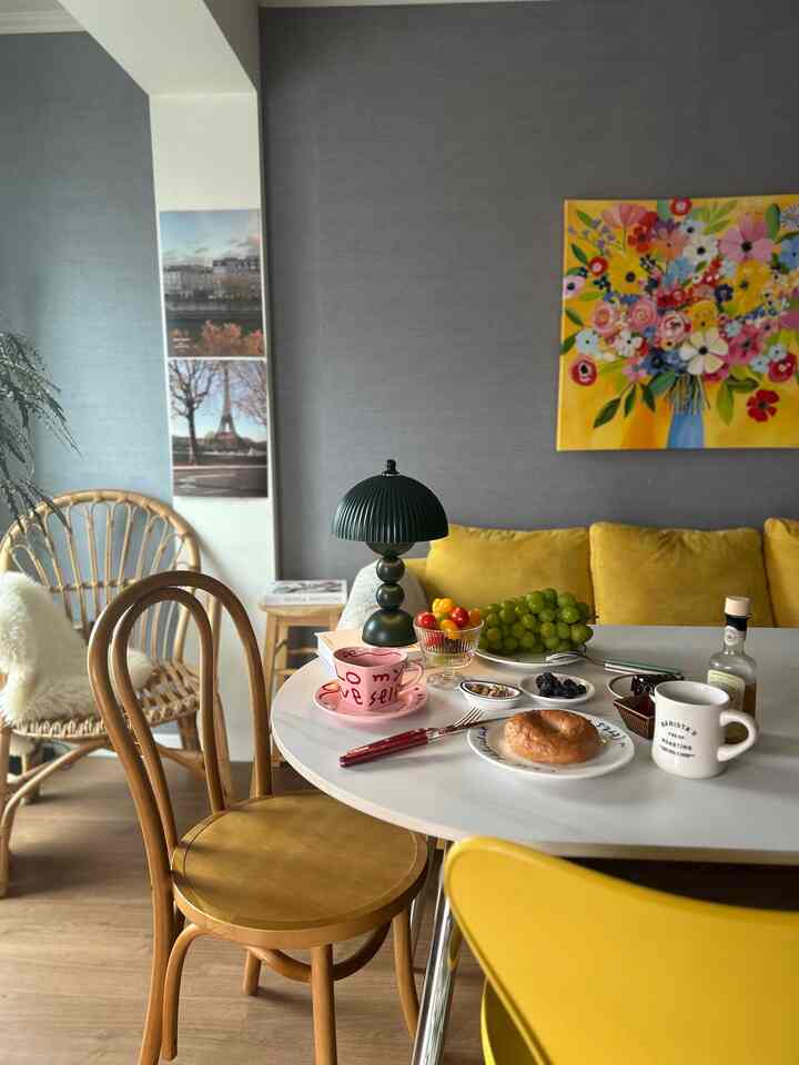 Dining room with gray walls and yellow sofa, featuring a white dining table, wooden chairs, and home cafe style table lamp with mugs