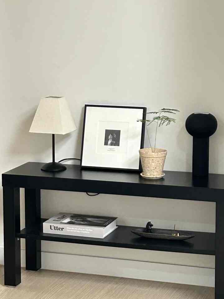 Black-toned bench featuring table lamp, framed art, and vase arranged as simple objets in a modern setting
