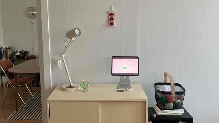 ホワイトとベージュ調のホームオフィス空間、クリーム色のキャビネットとタブレットスタンド、テーブルランプが配置されたシンプルでモダンなインテリア