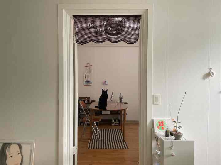 白い壁と木目調の床が調和したリビング、木製のダイニングテーブルに座る黒い猫が印象的なナチュラルなインテリア