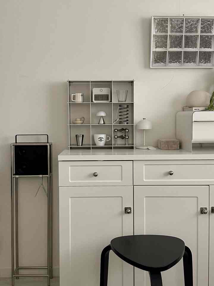 明るいホワイトトーンのキッチン収納スペース、黒いスツールとイケアのスピーカーが配置された、清潔感のあるモダンなインテリア