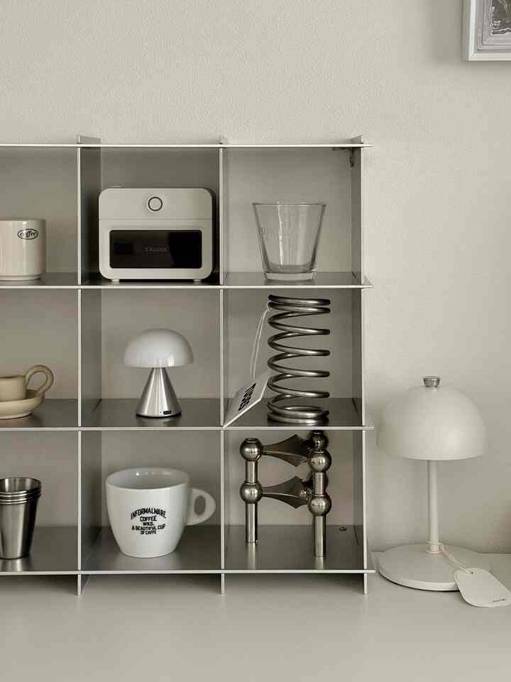 ホワイトとメタリックトーンの収納棚とテーブルランプが配置されたミニマルな空間