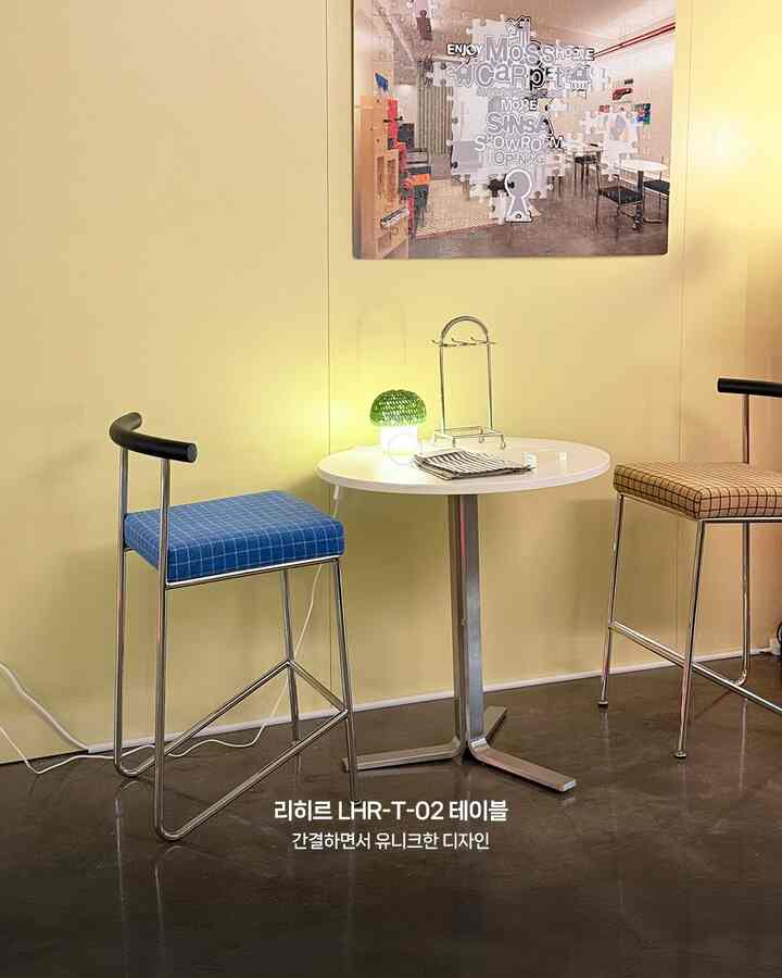 黄色の壁を背にしたコンパクトなおうちカフェ、丸い白いテーブルと青と茶色のスツールが配置されたモダンなインテリア