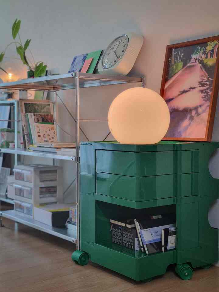 Modern space featuring a green cabinet and silver stainless steel shelves, accented by a spherical lamp and wall clock