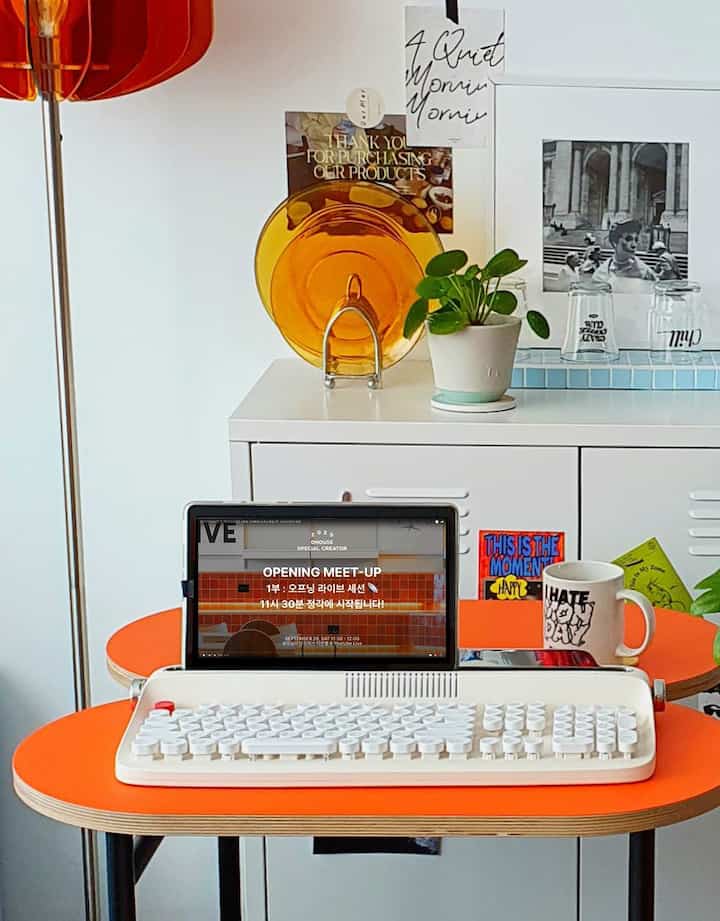 白とオレンジのトーンのホームオフィス空間、レトロなキーボードとオレンジ色のダイニングテーブルが配置され、温かみのある雰囲気のインテリア
