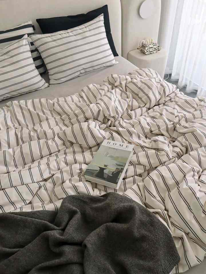 White and black striped bedding in bedroom featuring table lamp and side table, creating a clean and calm atmosphere
