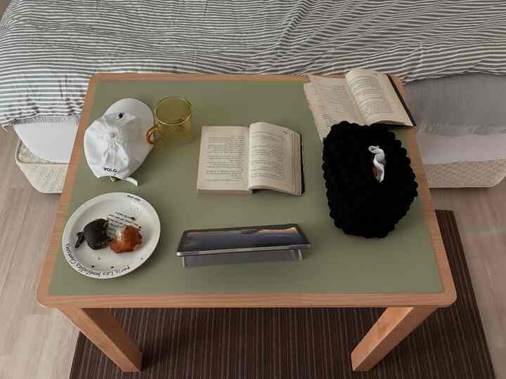 オリーブ色のテーブルマットが敷かれたナチュラルトーンのデスクに本や帽子、皿が置かれた居心地の良いリビング空間