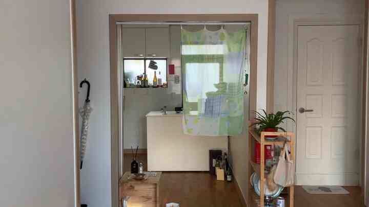 ホワイトの壁と木目調の床のコンパクトなワンルーム、ナイトテーブルとディフューザーが配置された温かみのあるキッチン入口