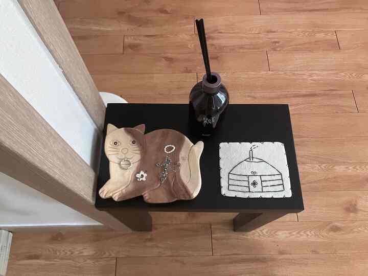 木目調の床と黒いスツールに置かれた猫型の木製トレイとディフューザーがある、雰囲気のある玄関空間
