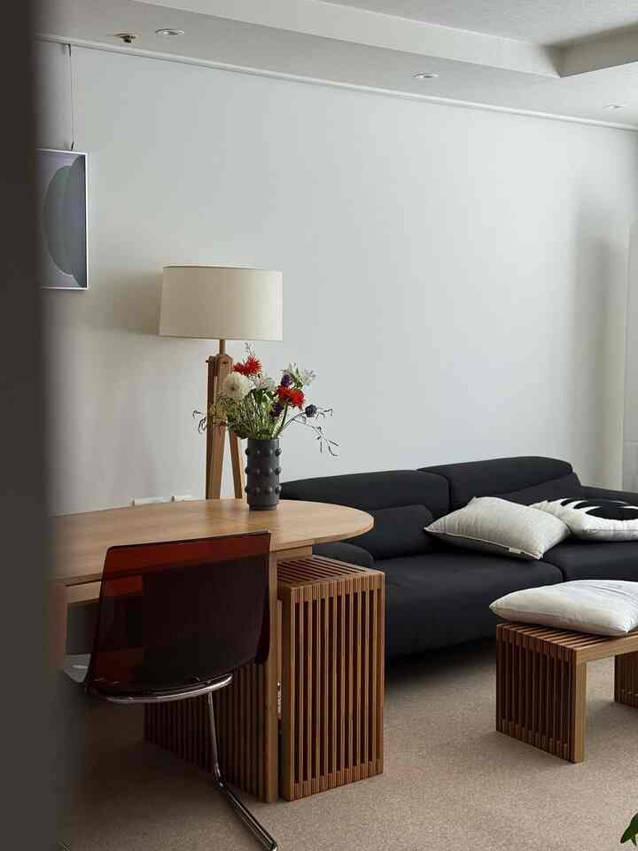 白い壁と木目調家具が調和したモダンでシンプルな4人暮らし向けリビング、黒いソファと照明を配置
