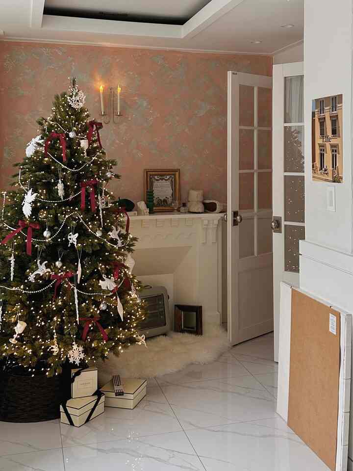 温かみのあるホワイトとブラウンの玄関スペース、180cmのクリスマスツリーと装飾品、壁付け照明が配置された落ち着いた雰囲気のインテリア