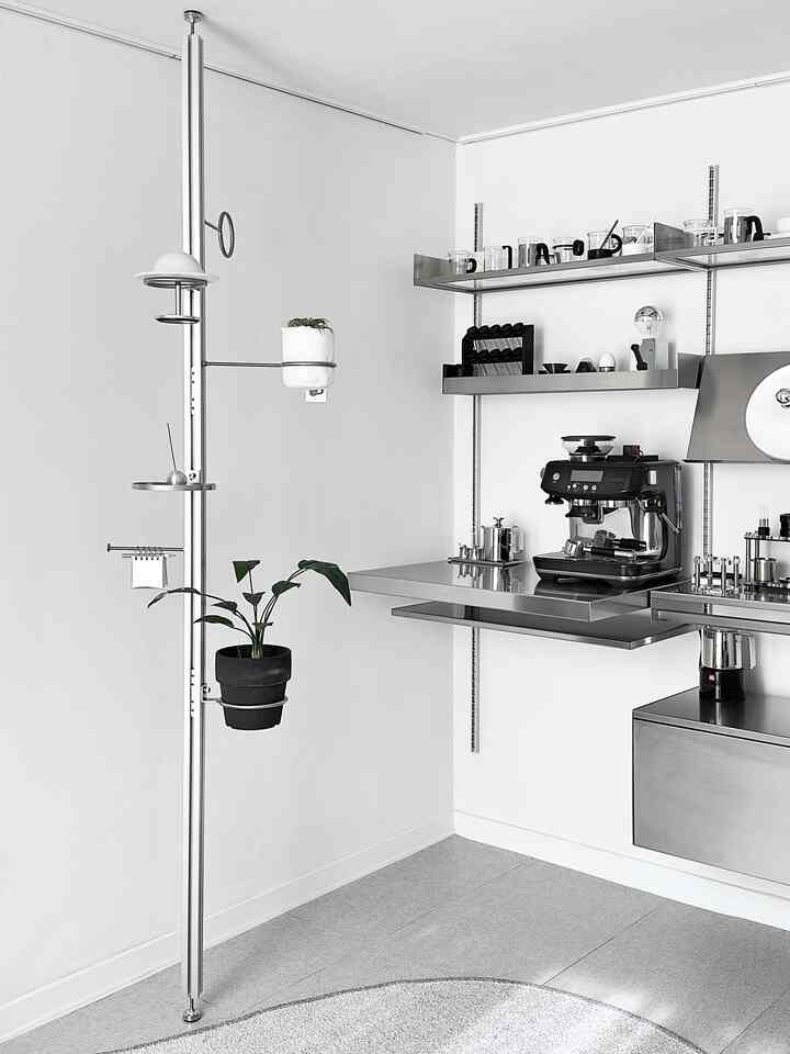 モノトーンの小さなホームカフェ空間、ステンレス製ハンガーと棚、コーヒーマシンと植物が調和したモダンなインテリア