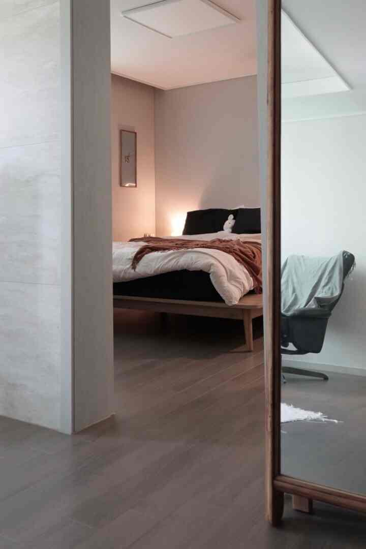 柔らかいナチュラルトーンと黒・白が調和した6畳の寝室、木製ベッドフレームとリクライニングチェアが配置された落ち着いた空間