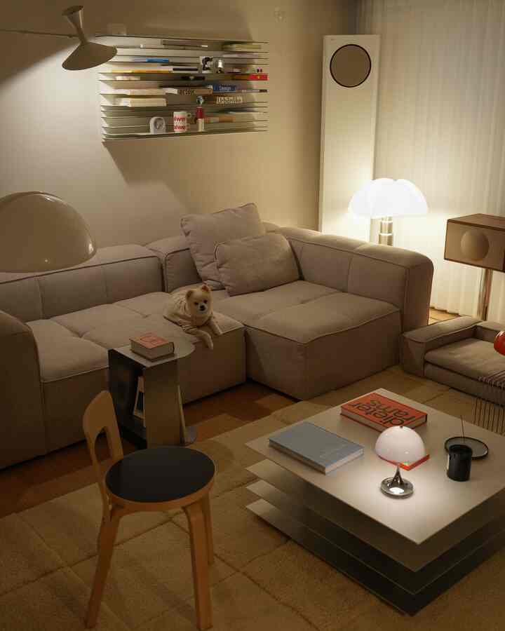 ベージュとウッドトーンの北欧風リビング、大きなソファに犬とテーブルランプ、フロアランプが配置された落ち着いた空間