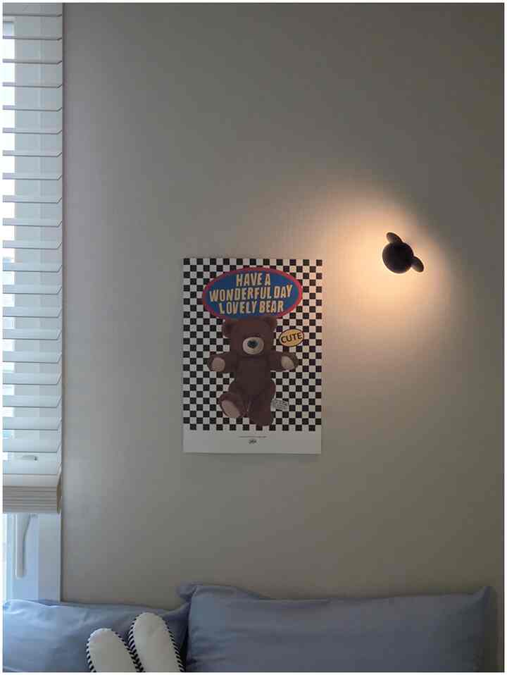 ベージュ調の子供部屋、ホワイトのブラインド、ミッキー形の無線壁ライトとかわいいテディベアのポスターが配置された落ち着いた雰囲気のインテリア