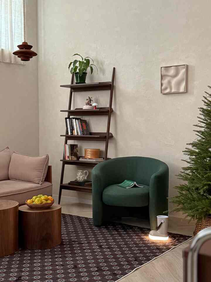 落ち着いたグリーンのソファとナチュラルなベージュの壁、木製の棚とクリスマスツリーが配置された雰囲気のある冬のリビングルーム