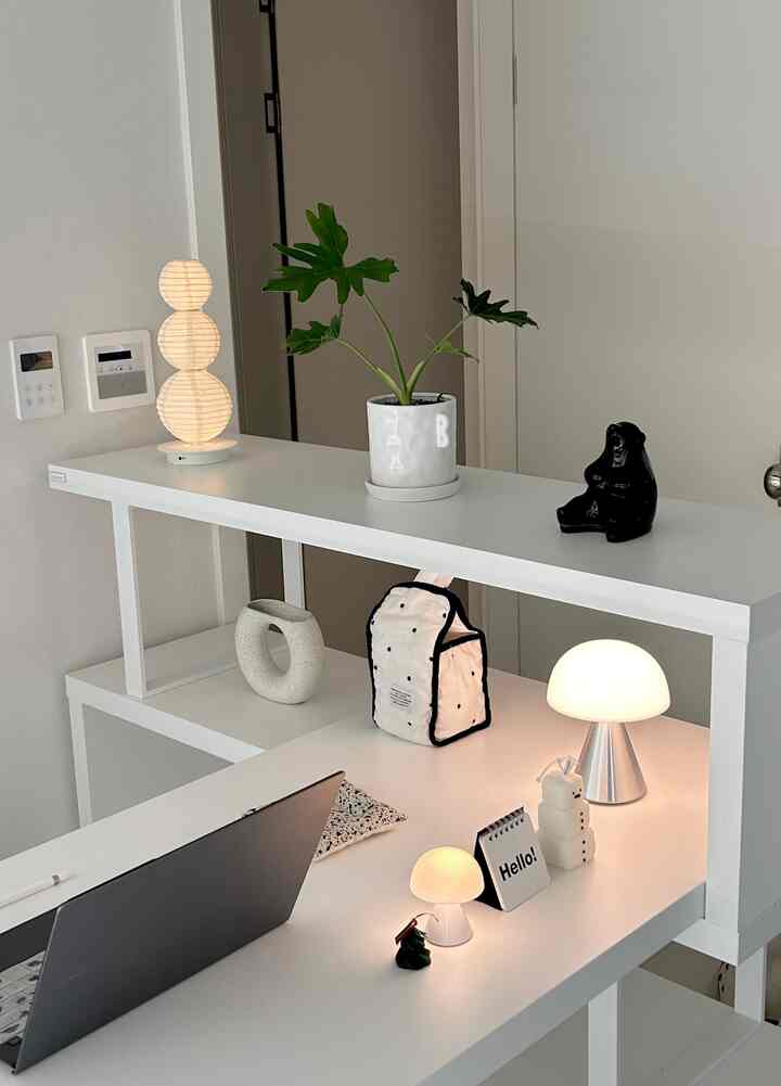 ホワイトトーンの玄関空間、植物と個性的なオブジェが配置されたミニマルで清潔感のあるテーブルランプ空間
