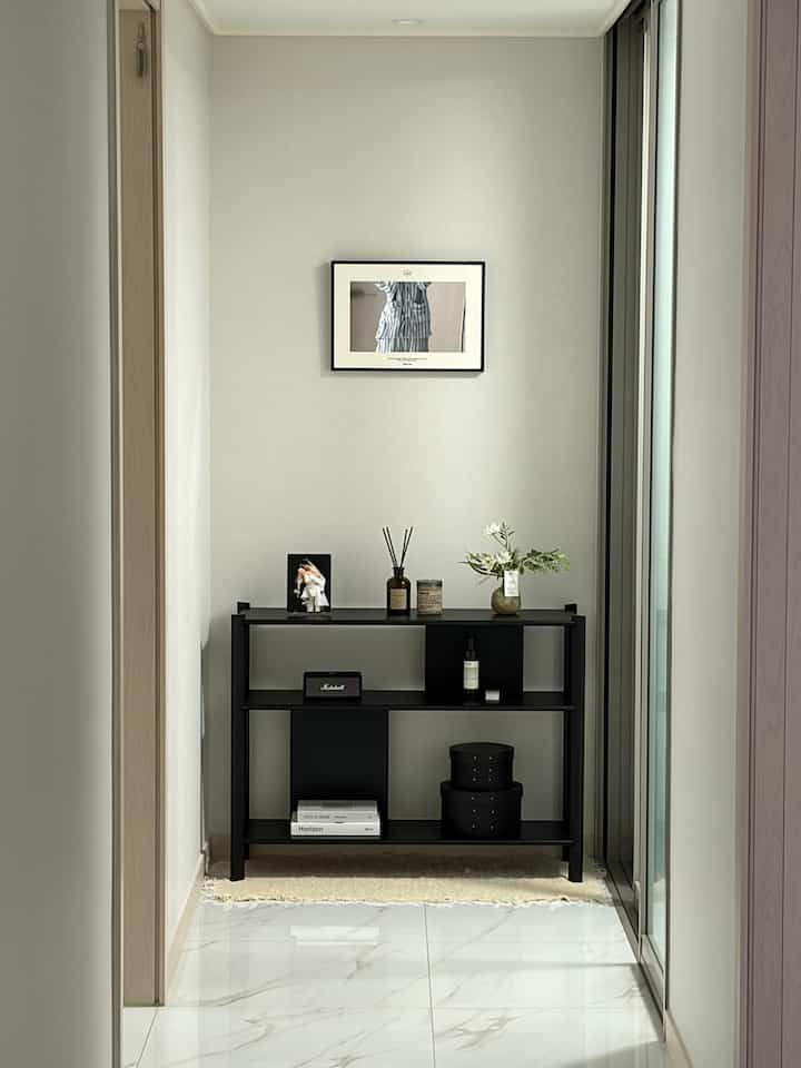 白い壁と床、黒い3段シェルフが中央に配置された狭い廊下空間で、ミニマルで清潔感のあるインテリア