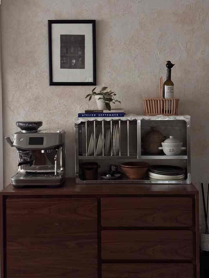 ヴィンテージレースクロスとテラコッタ鉢が置かれた木製キャビネットの上にステンレス製のキッチンラックとエスプレッソマシンがある温かみのあるキッチンスペース
