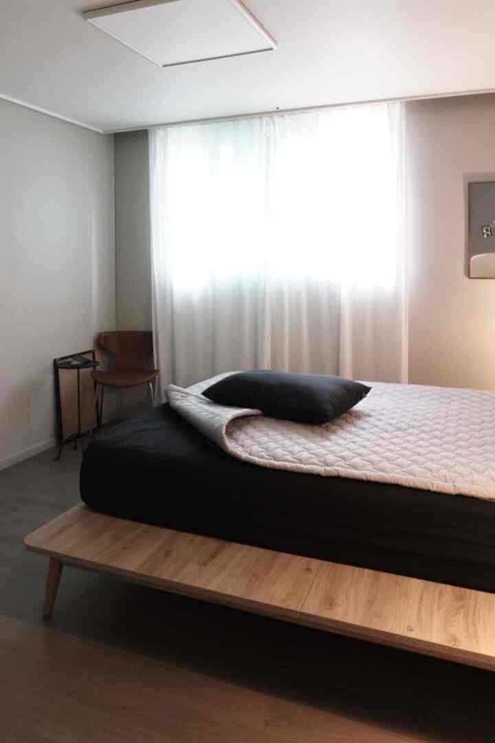 ナチュラルカラーとモダンスタイルが調和した寝室、木製ベッドフレームと黒いマットレスが配置されたシンプルな印象的な空間