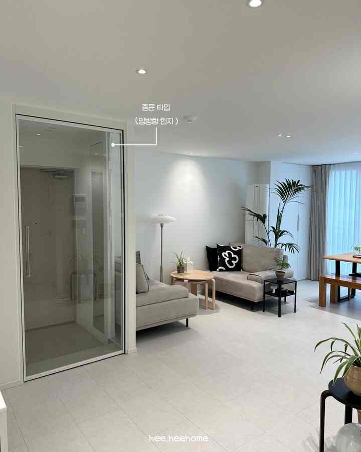 白と透明ガラスの玄関とリビング空間、スリムフレームの中間扉とモダンな家具が配された印象的なシンプルインテリア