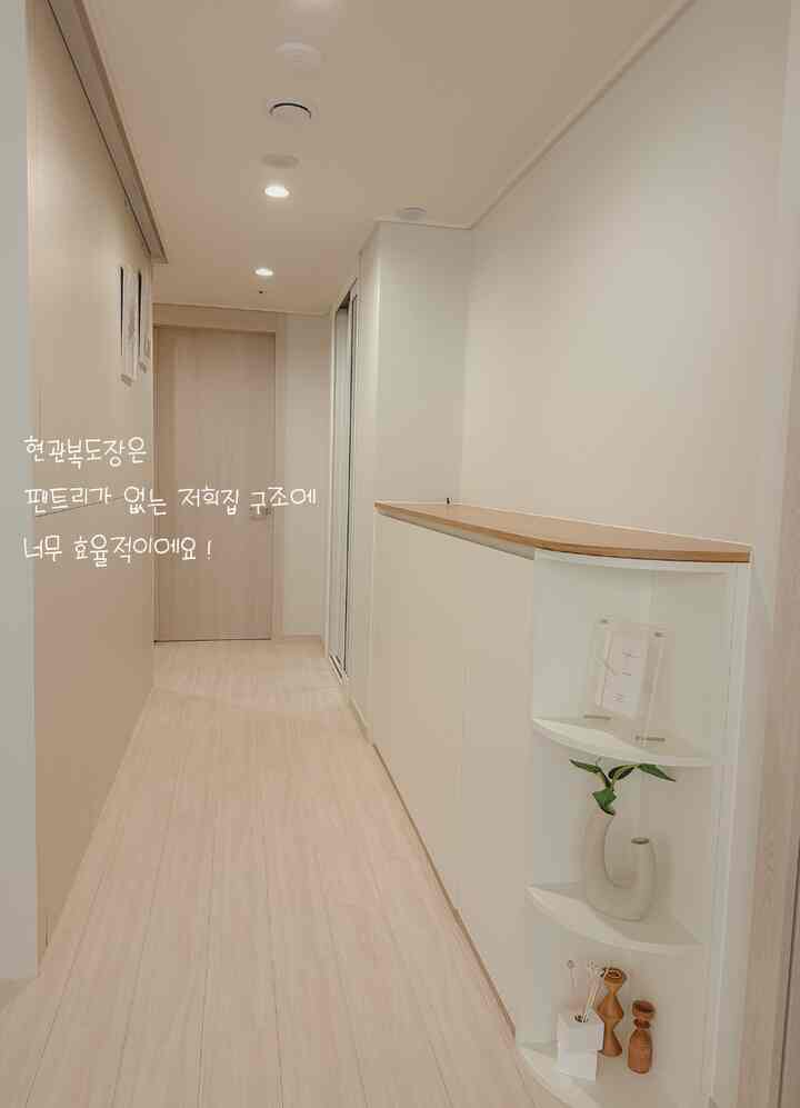 白とライトブラウンの色調の玄関廊下、すっきりとした高い収納家具とコーナー棚にオブジェが配置されたシンプルなインテリア