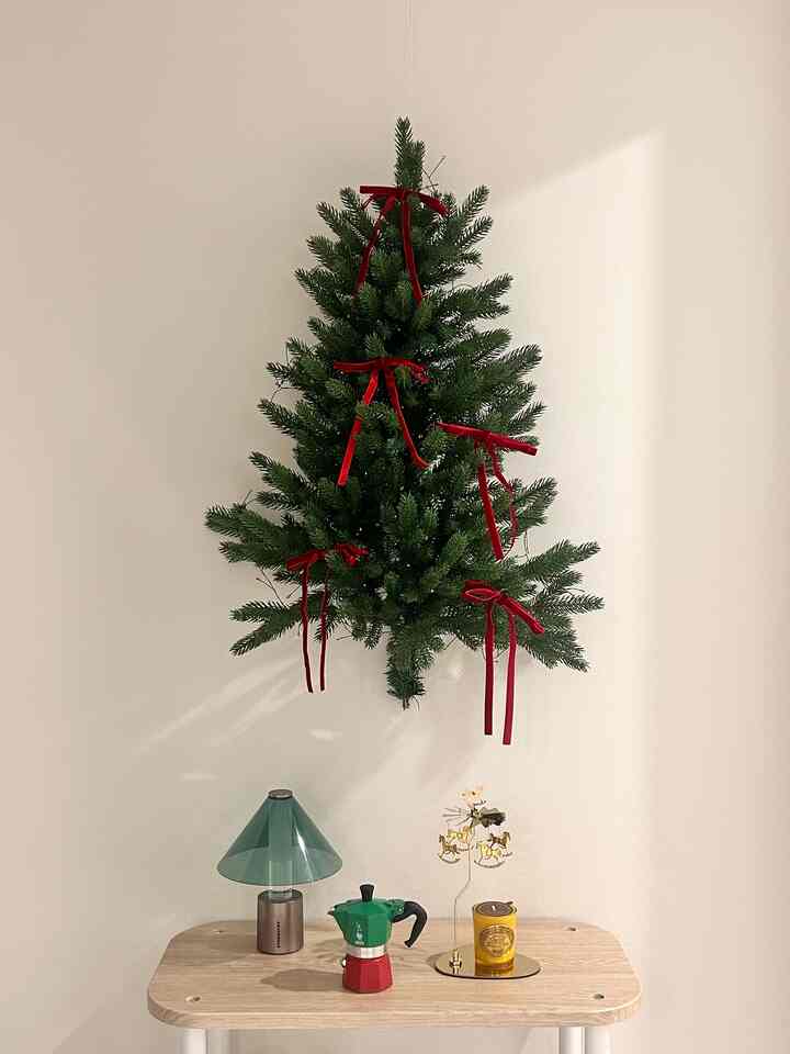 Natural tone minimalist space with a small hanging Christmas wall tree, featuring a wooden table with a moka pot and mood lamp