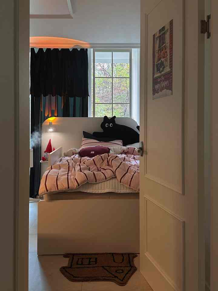 ホワイトとピンクの色調の6畳の寝室、白いベッドとピンクの寝具、黒いカーテンと窓が配置された印象的な空間