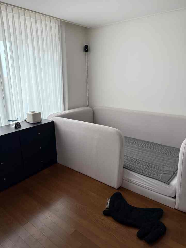 淡いモノトーンの子供部屋、スーパーシングルのベビーベッドとダークなチェストが配置されたすっきりとしたインテリア