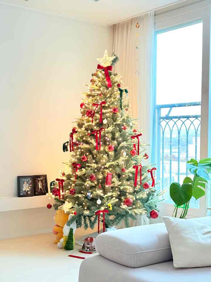 明るい白とベージュの色調のリビング、高く飾られた緑のクリスマスツリーと赤いリボンが配置された上品なインテリア