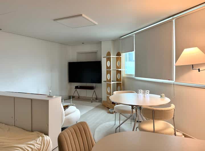 白とベージュのトーンのワンルーム、丸いダイニングテーブルとキャットタワーが配置された雰囲気のあるインテリア