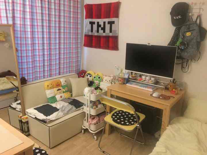 パステル調のチェックカーテンとライトブラウンの木製デスクがある、一人暮らし向けのコンパクトなホームオフィスとソファの空間