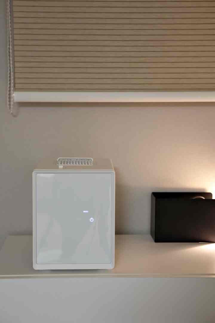 白とベージュの色調の玄関、シンプルなインテリアにキューブ型の家電とブラインドが配置された空間