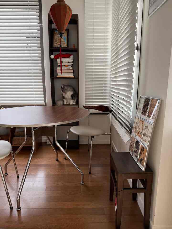 明るい白いブラインドと茶色の丸いダイニングテーブル、椅子が配置されたナチュラルな雰囲気のリビングスペース