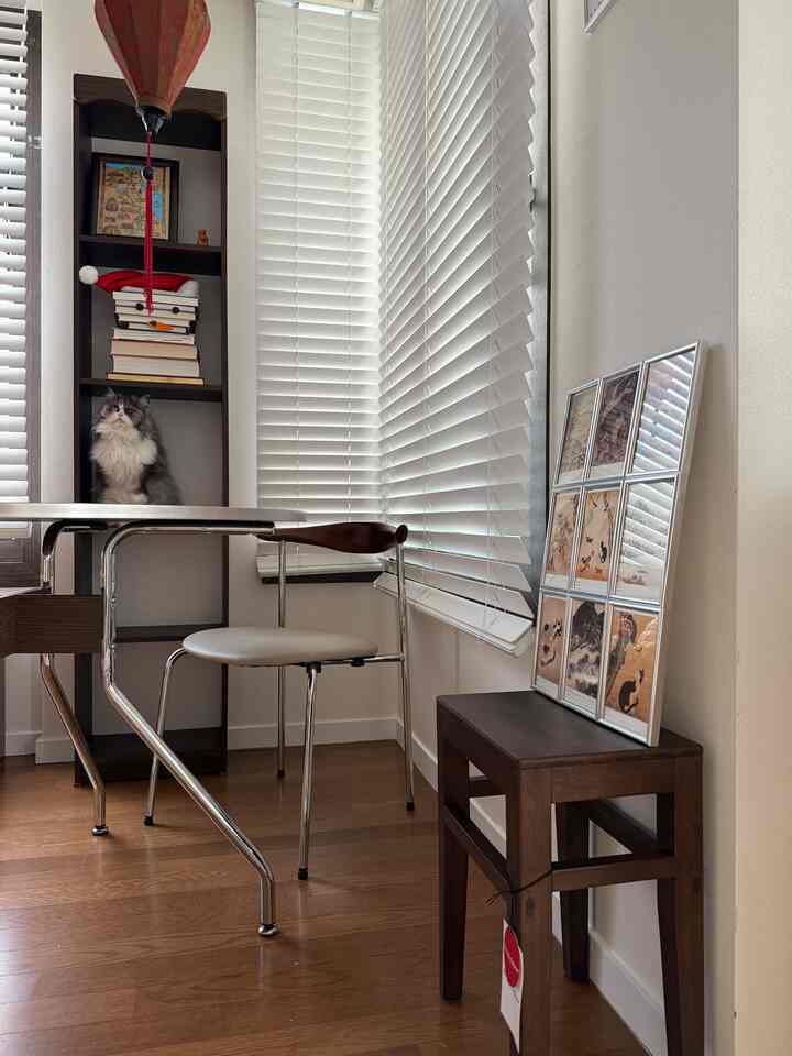 ホワイトとウッドトーンのリビングルーム、ミッドセンチュリーモダンチェアとスツール、猫と額縁が配置された雰囲気のあるインテリア