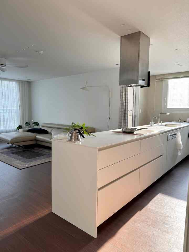 ホワイトとブラウンのトーンの自然なモダンなリビングとキッチン、広いキッチンアイランドとベージュのコーナーソファが配置された印象的な空間