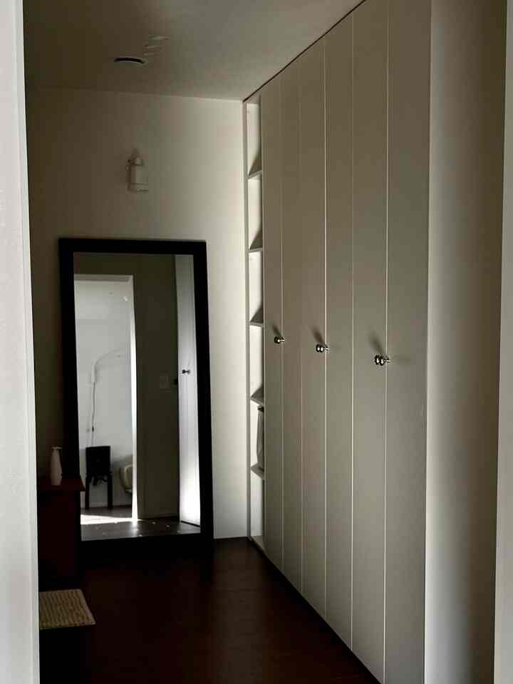 白い壁とビルトインクローゼット、木目調の床が調和した廊下型ウォークインクローゼット、大型イケア鏡と照明が印象的な空間