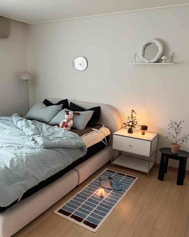 白と青の色調が調和した寝室、居心地の良いベッドと小さなラグ、暖かな照明がある雰囲気のあるインテリア